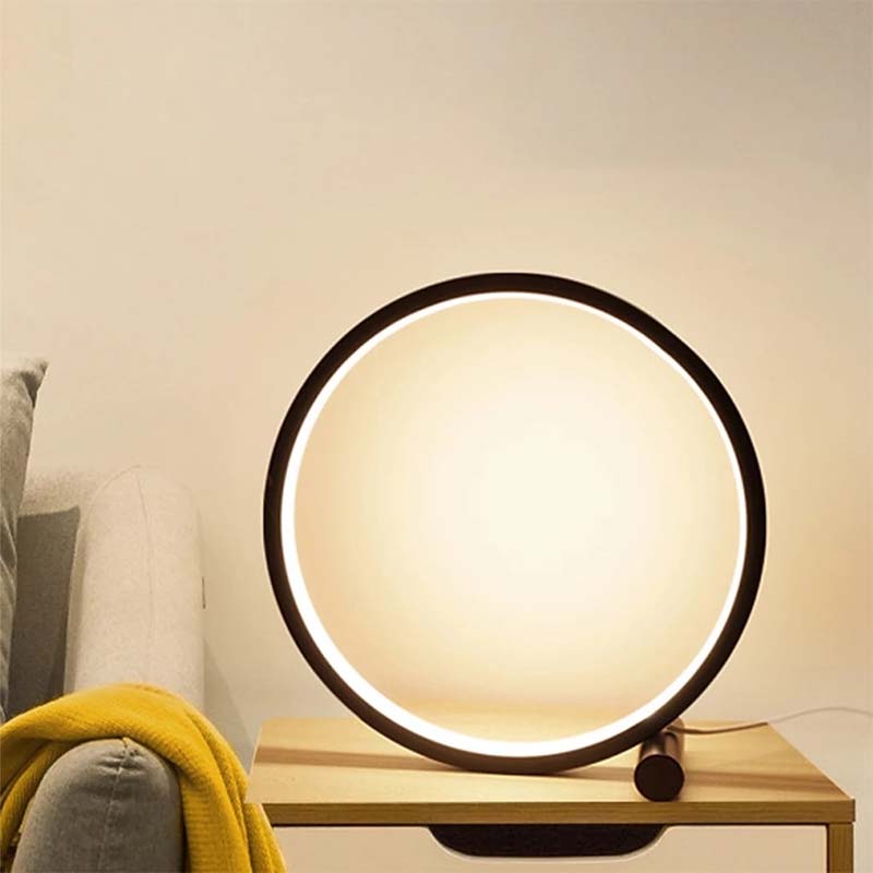 Round table lamp with a black frame on a wooden surface, emitting a warm glow.