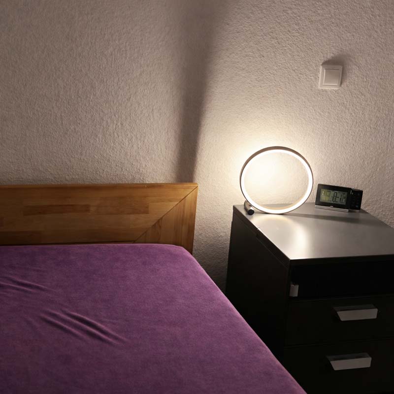 Bedroom with a wooden headboard and purple bedspread, nightstand with lamp and clock.