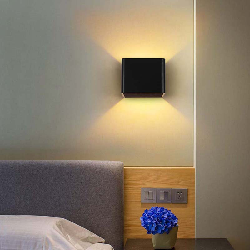 Wall-mounted square light fixture on a bedroom wall with a bed and flowers in the foreground.