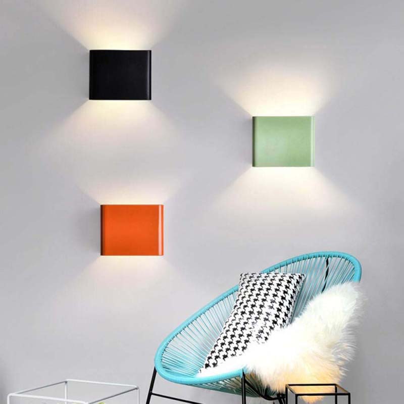 Modern wall lights in black, green, and orange on a white wall with a blue chair and decorative pillows.