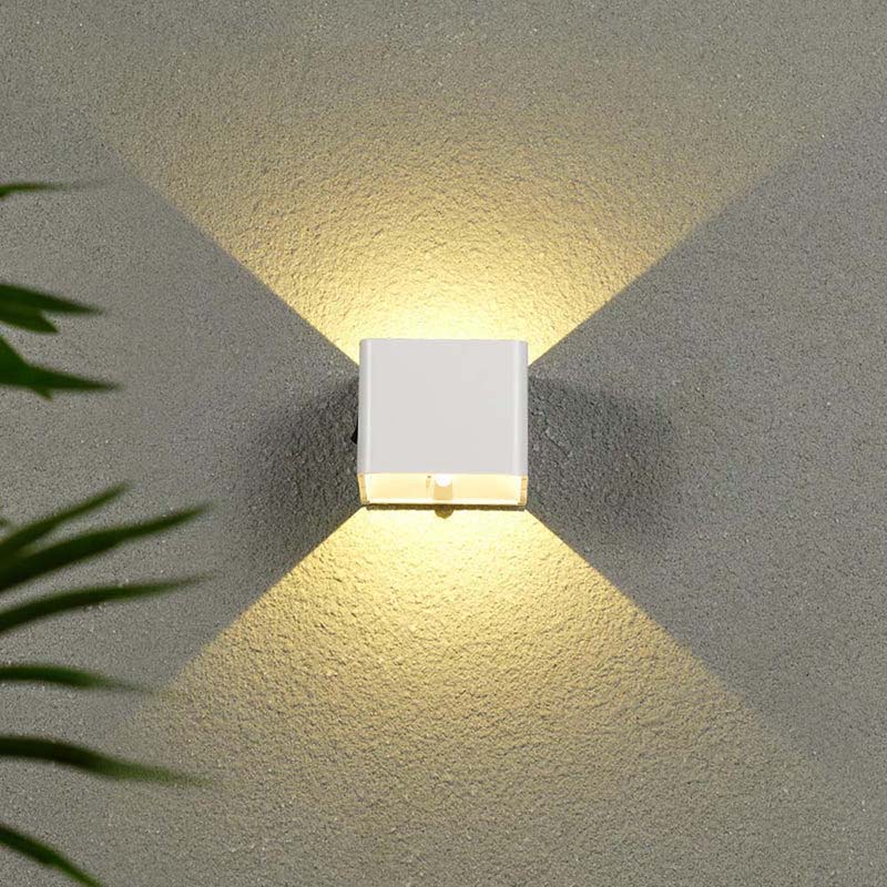 Square wall light fixture on a textured wall with plant leaves in the corner.