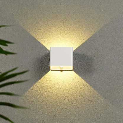 Square wall light fixture on a textured wall with plant leaves in the corner.