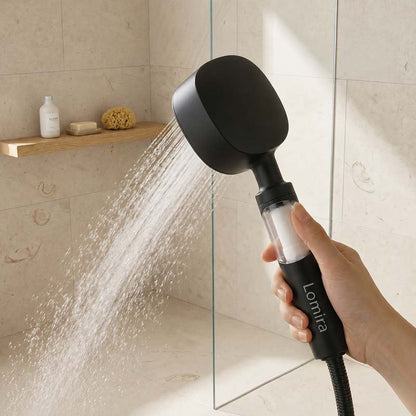 Black handheld shower head with water flowing from it, held in a person's hand in the bathroom.