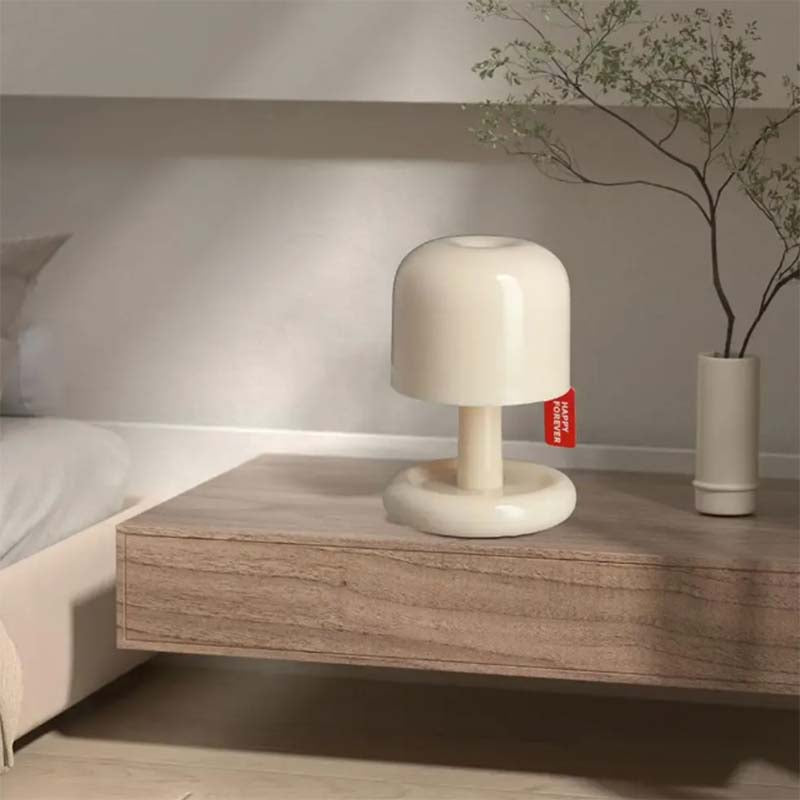 Beige lamp on a wooden nightstand with a plant in the background