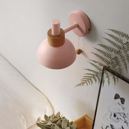 Pink wall lamp with wooden accent on a light-colored wall.