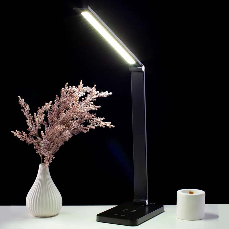 Black LED desk lamp on a white surface with a vase and candle against a black background
