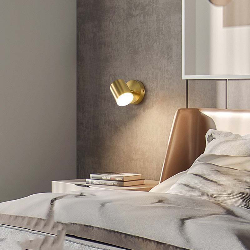 Gold wall sconce on a textured wall above a bed with white bedding.