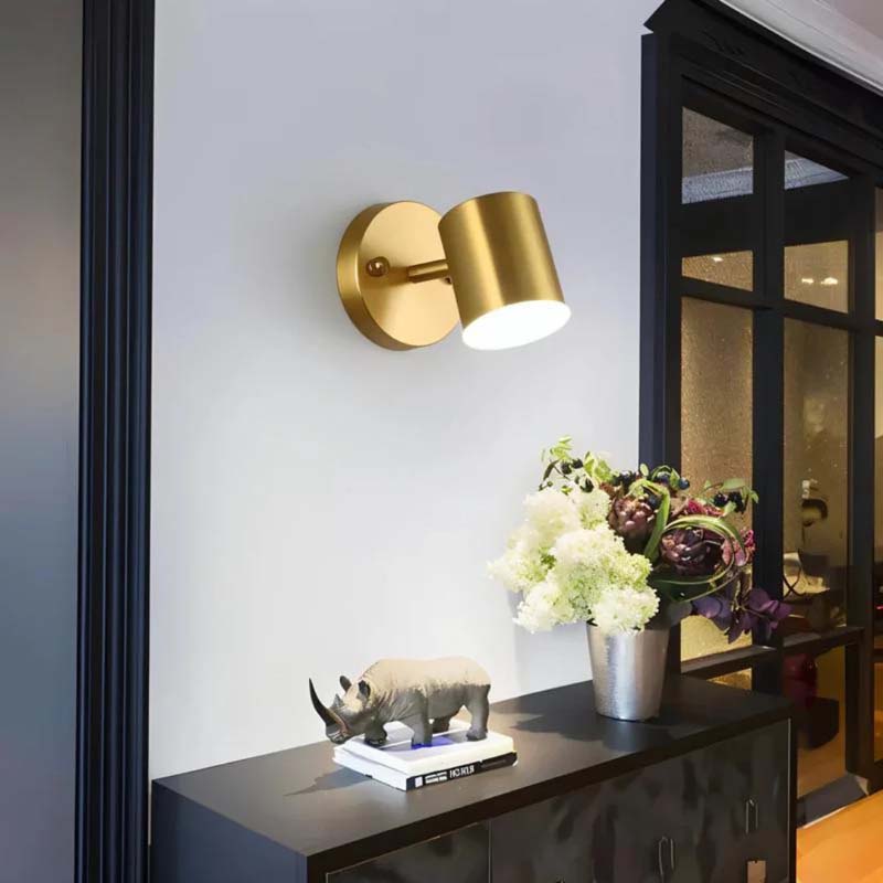 Gold wall sconce on a white wall with decorative items on a shelf below.