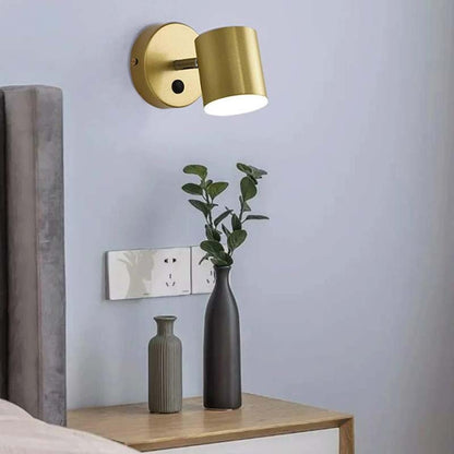 Gold wall sconce on a light blue wall with decorative vases and a plant.