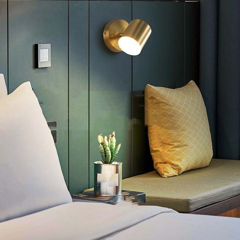 Gold wall sconce above a bed with pillows and a small plant.