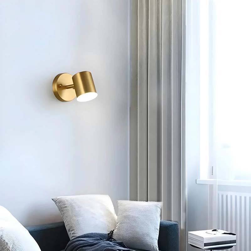 Gold wall sconce on a white wall with a couch and window in the background