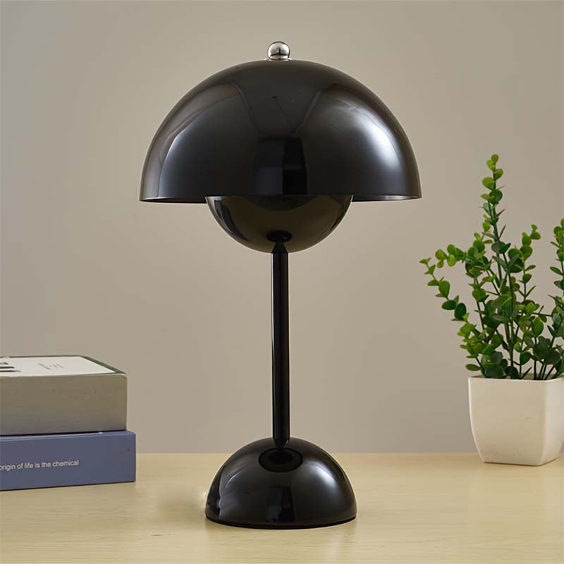 Black table lamp on a wooden surface with a plant and books in the background