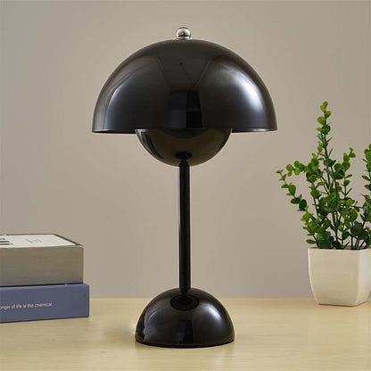 Black table lamp on a wooden surface with a plant and books in the background