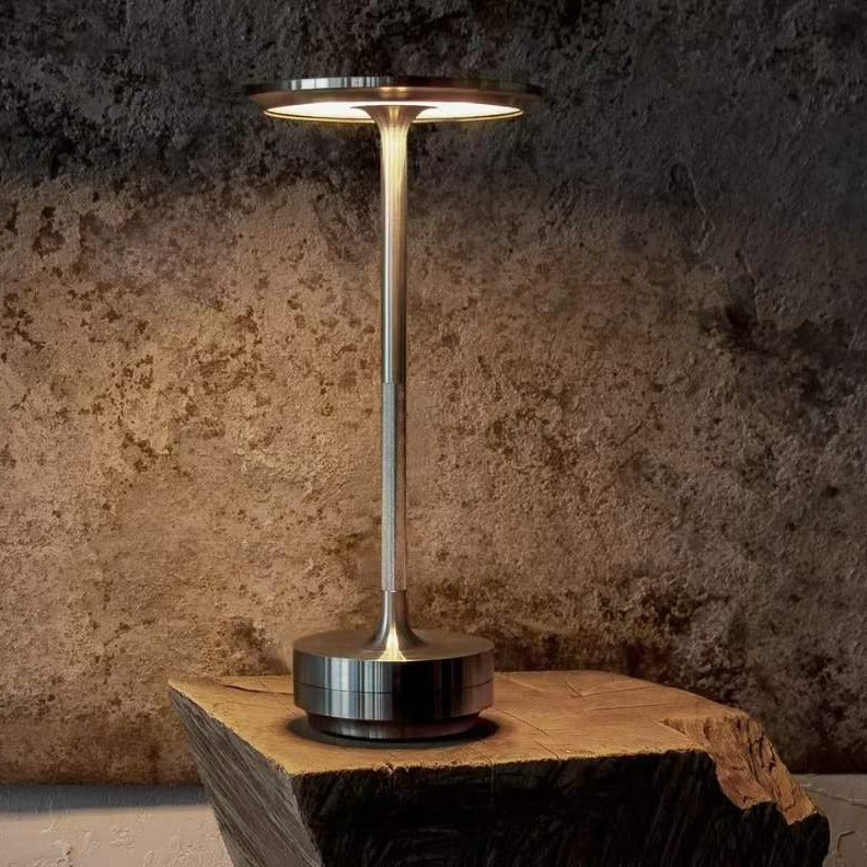 Modern table lamp with metallic base and cylindrical shade on a wooden surface against a textured wall.