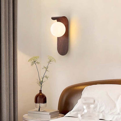 Wall-mounted lamp and vase with flowers on a nightstand in a bedroom setting.