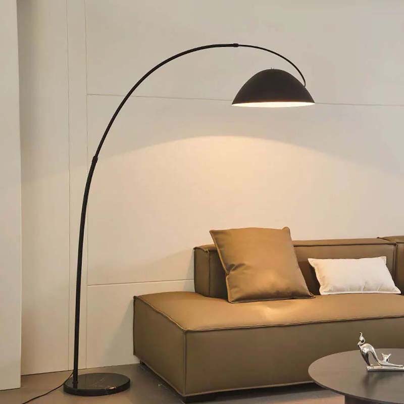 Modern arc floor lamp with a black dome shade placed beside a sofa.