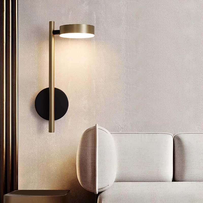 Modern wall lamp with gold finish on a textured wall next to a white sofa.