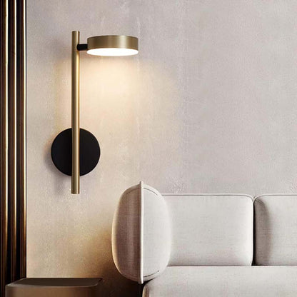 Modern wall lamp with gold finish on a textured wall next to a white sofa.