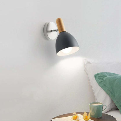 Wall-mounted lamp with wooden accent on a light gray wall, next to a table with a mug and flowers.