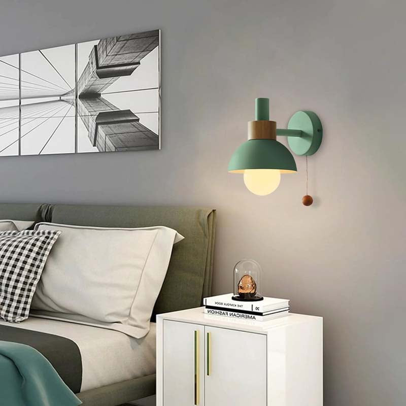 Green wall lamp above a white cabinet with books and a decorative item in a bedroom setting.