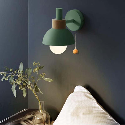 Green wall lamp on a dark wall with a vase of leaves and blanket in the foreground