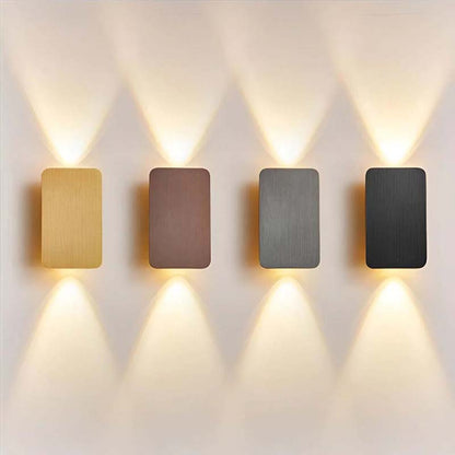 Four rectangular wall lights in gold, bronze, silver, and black on a white wall.