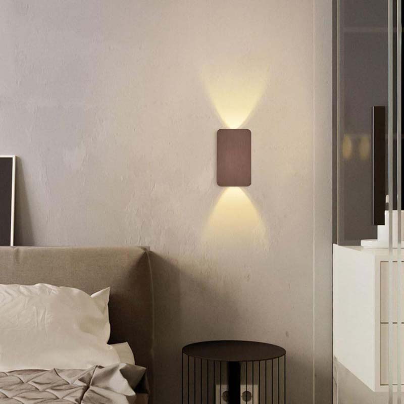 Wall-mounted light fixture on a bedroom wall with a bed and nightstand in the foreground.