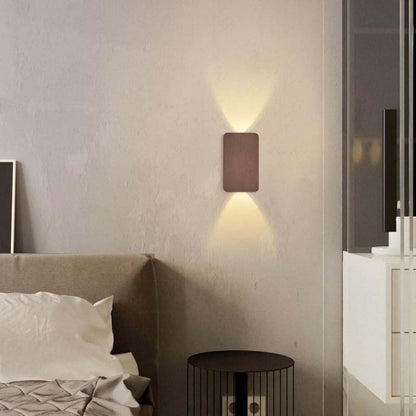 Wall-mounted light fixture on a bedroom wall with a bed and nightstand in the foreground.