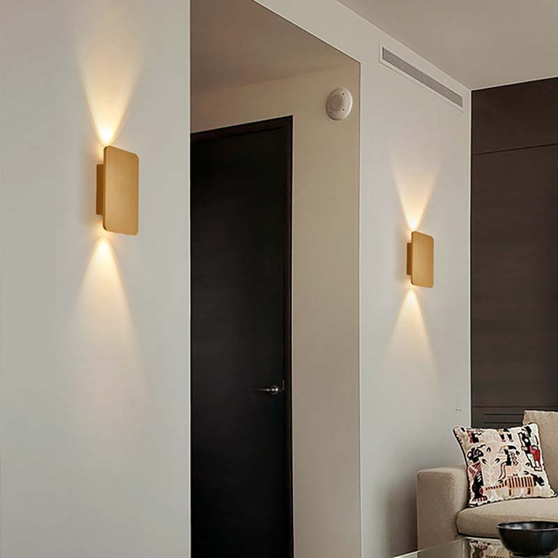 Modern wall lights on a white wall with a dark door and a chair with a decorative pillow in the background.