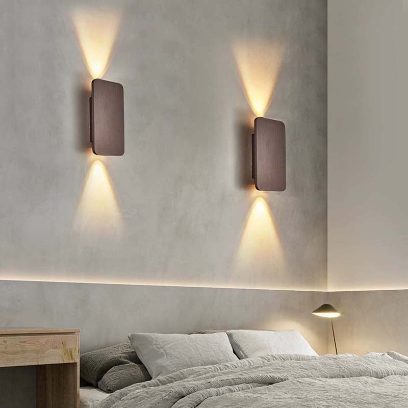 Modern wall lights on a concrete wall above a bed in a bedroom setting.