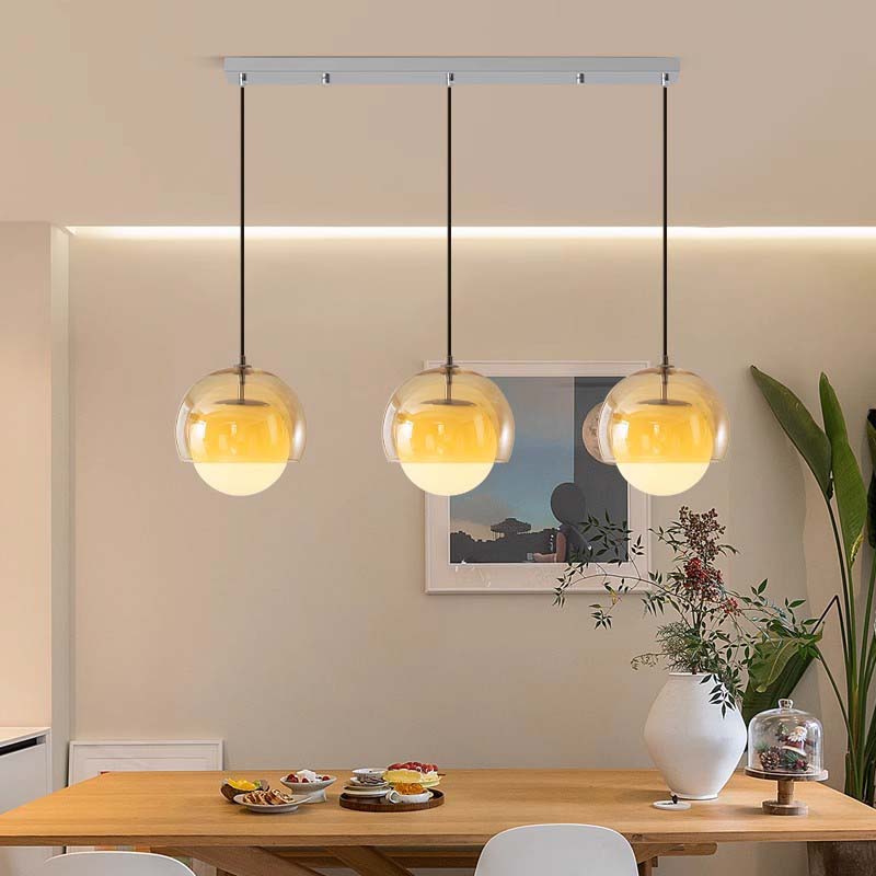 Modern pendant lights hanging above a dining table with a neutral wall and decor in the background.