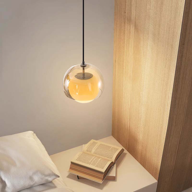 Pendant light with a warm glow on a wooden shelf next to an open book.