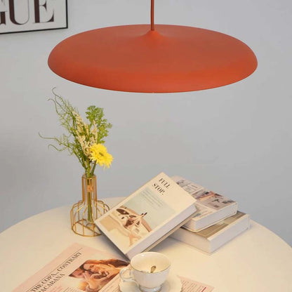 Red Pendant Lamp Luna. Macaron Pendant Light over a table with books, a cup, and flowers on a light gray background.