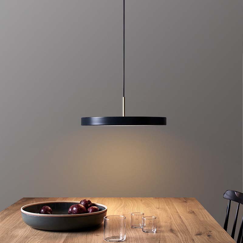Black pendant light hanging above a wooden table with a bowl of fruit and glasses.