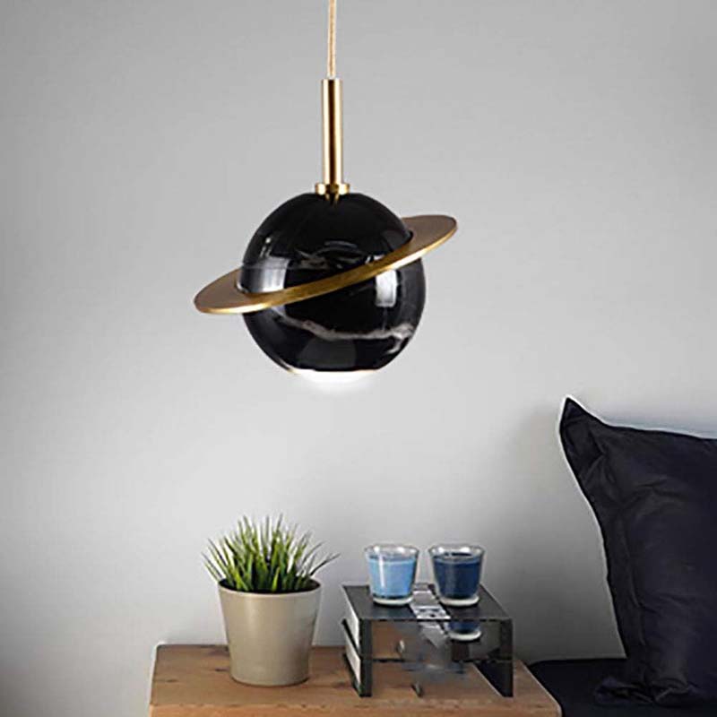 Modern black and gold pendant light fixture in a room setting with a plant and small table.