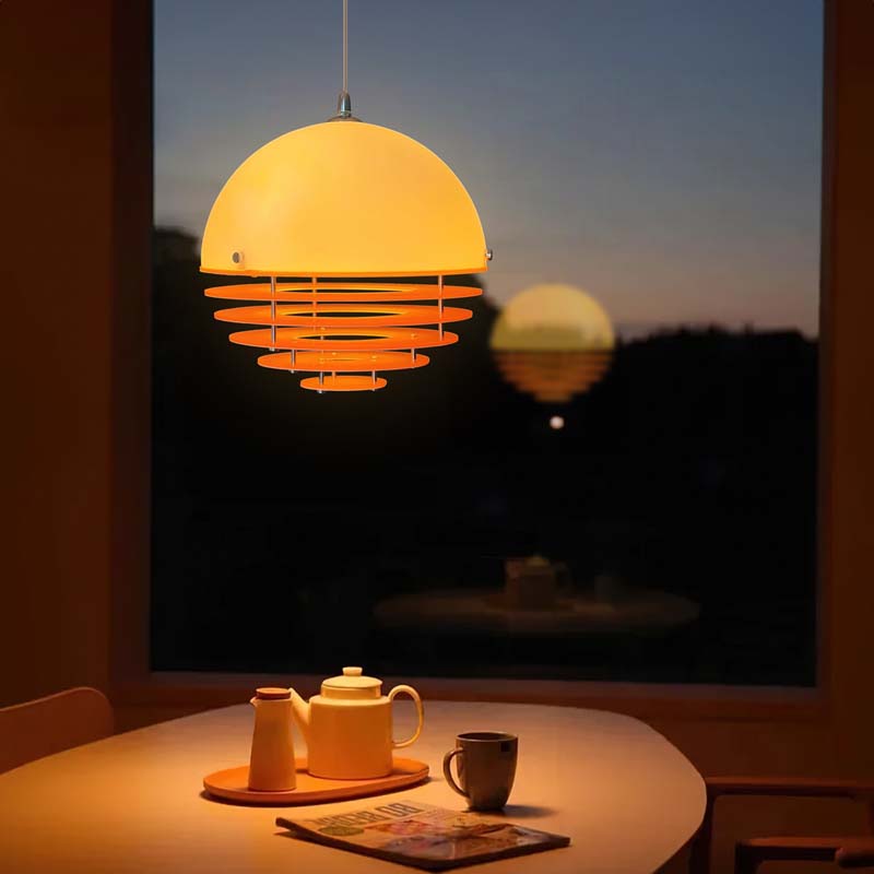 Pendant lamp Sunset with a dome-shaped shade above a table with a tea set by a window at sunset.