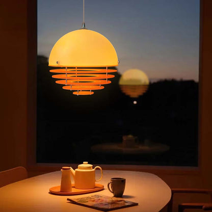 Pendant lamp Sunset with a dome-shaped shade above a table with a tea set by a window at sunset.