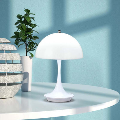 White table lamp on a round white table with a plant and decorative items against a light blue wall.