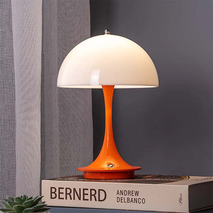 Table lamp with orange base and white shade on a book against a gray wall