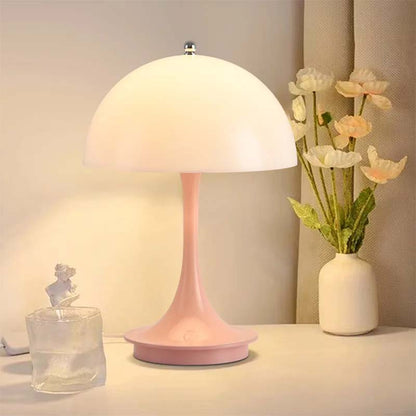 Pink table lamp on a surface with a vase of flowers and a glass container in the background.