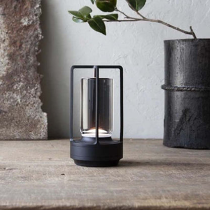 Modern outdoor lantern on a wooden surface with a plant in the background