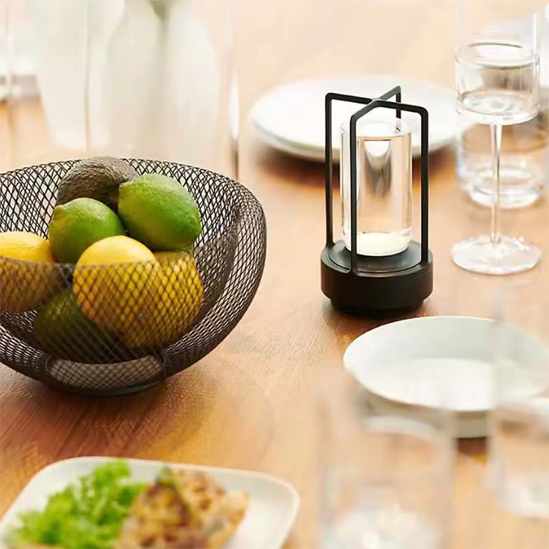 Bowl of fruit on a wooden table with a candle lantern and plates in the background