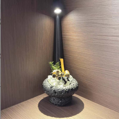 Decorative stone bowl with plants and table lamp on wooden table.