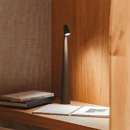Tall black lamp on a wooden surface with books and a textured wall in the background
