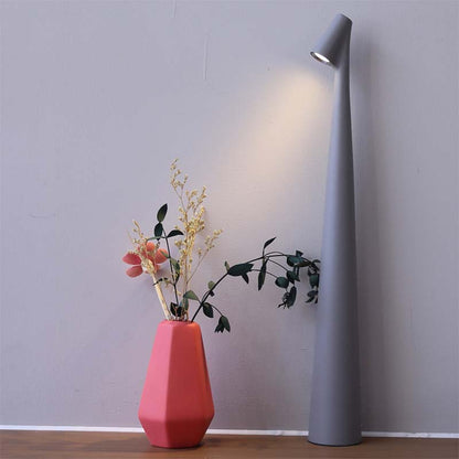 Modern table lamp and pink vase with flowers on wooden floor against gray wall background.