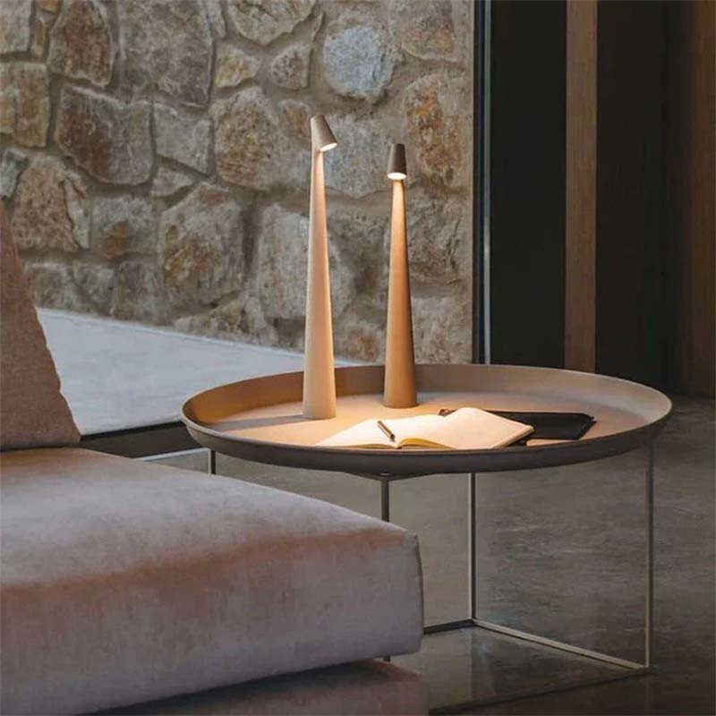 A round coffee table with two table lamps and an open book against a stone wall.