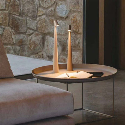 A round coffee table with two table lamps and an open book against a stone wall.
