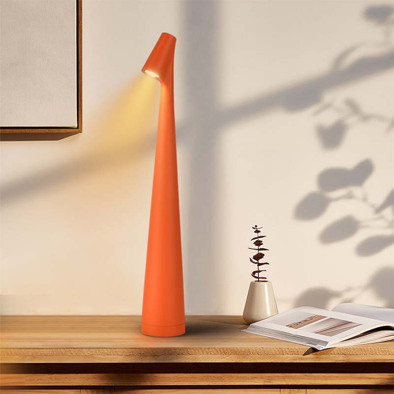 Orange cone-shaped lamp on a wooden surface with a plant and magazine in the background