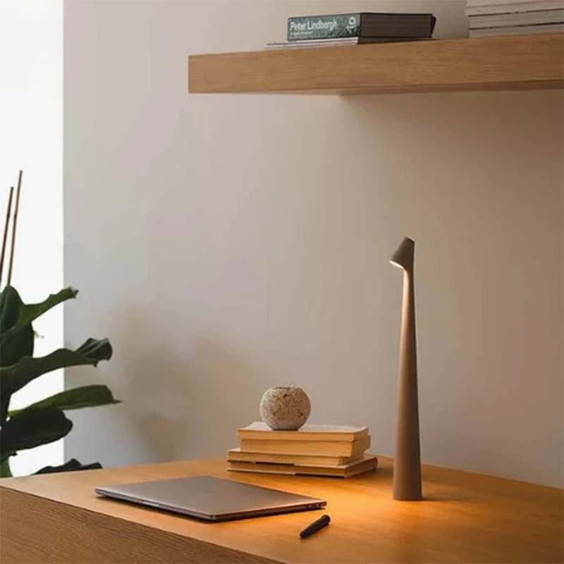 Wooden table with laptop, books and decorative table lamp against plain wall.