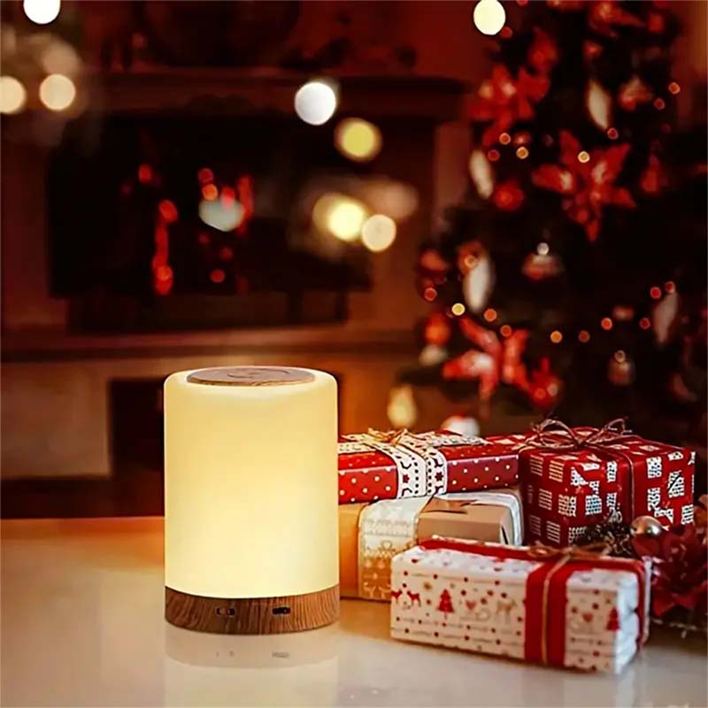 White lamp with wooden base on a table with wrapped gifts and a blurred Christmas tree in the background